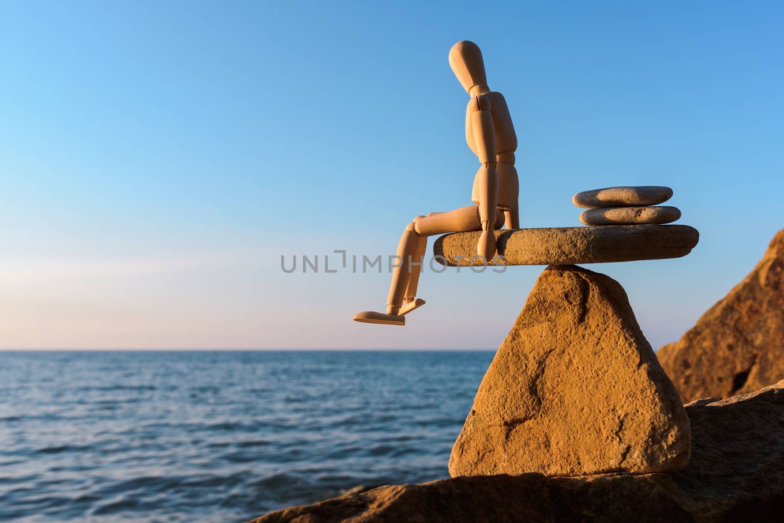 Wooden dummy sitting on the edge stone at the sea