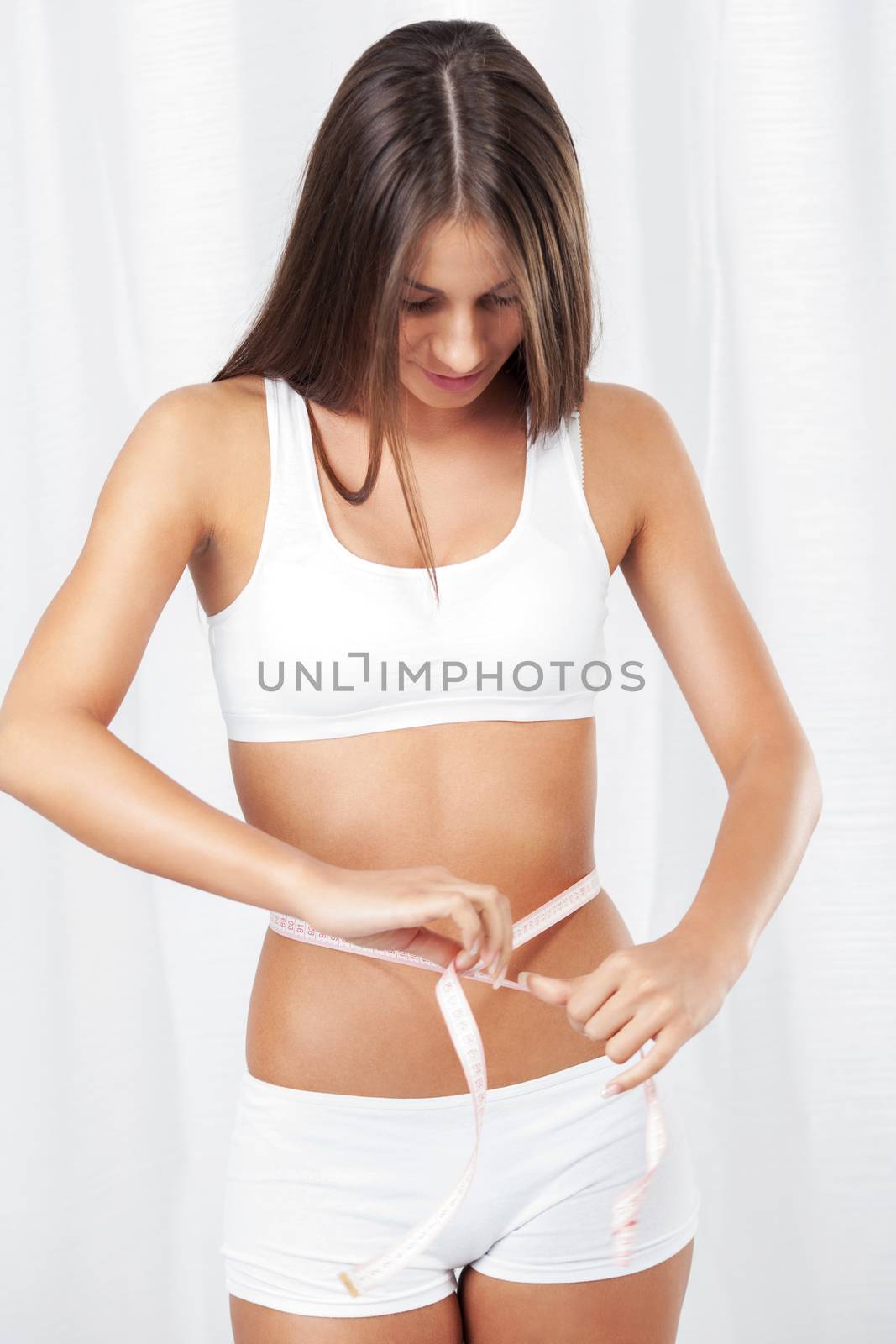 Beautiful young girl measuring perfect shape of waist.