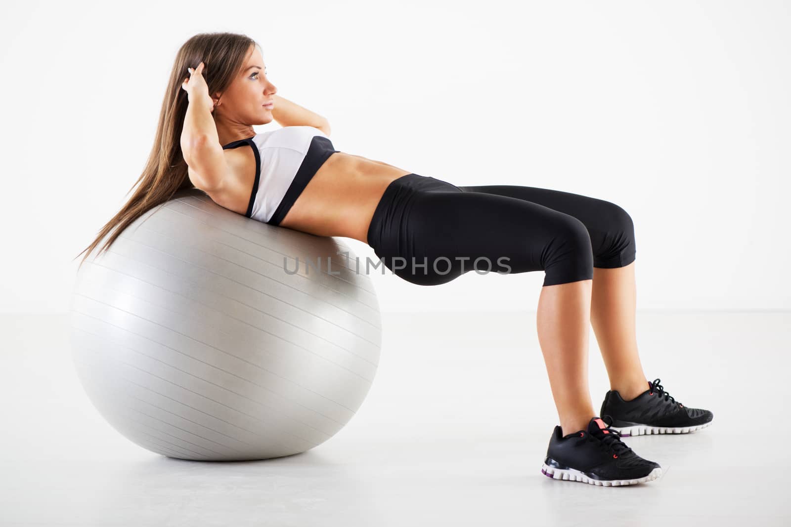 Young Beautiful Girl exercising and lifting the weights with Exercise Ball in Gym.
