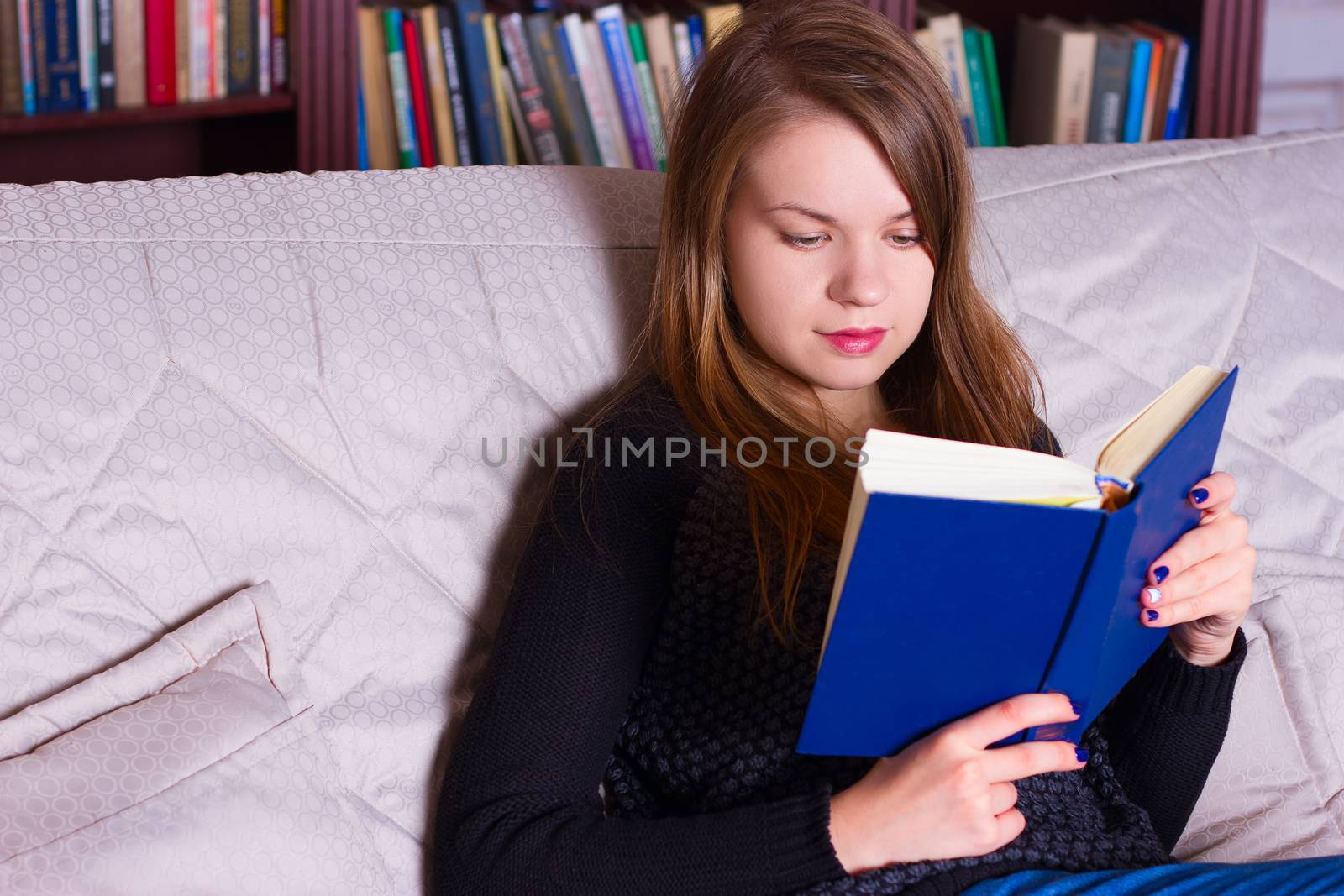 young woman sitting on sofa at home, reading a book  by victosha