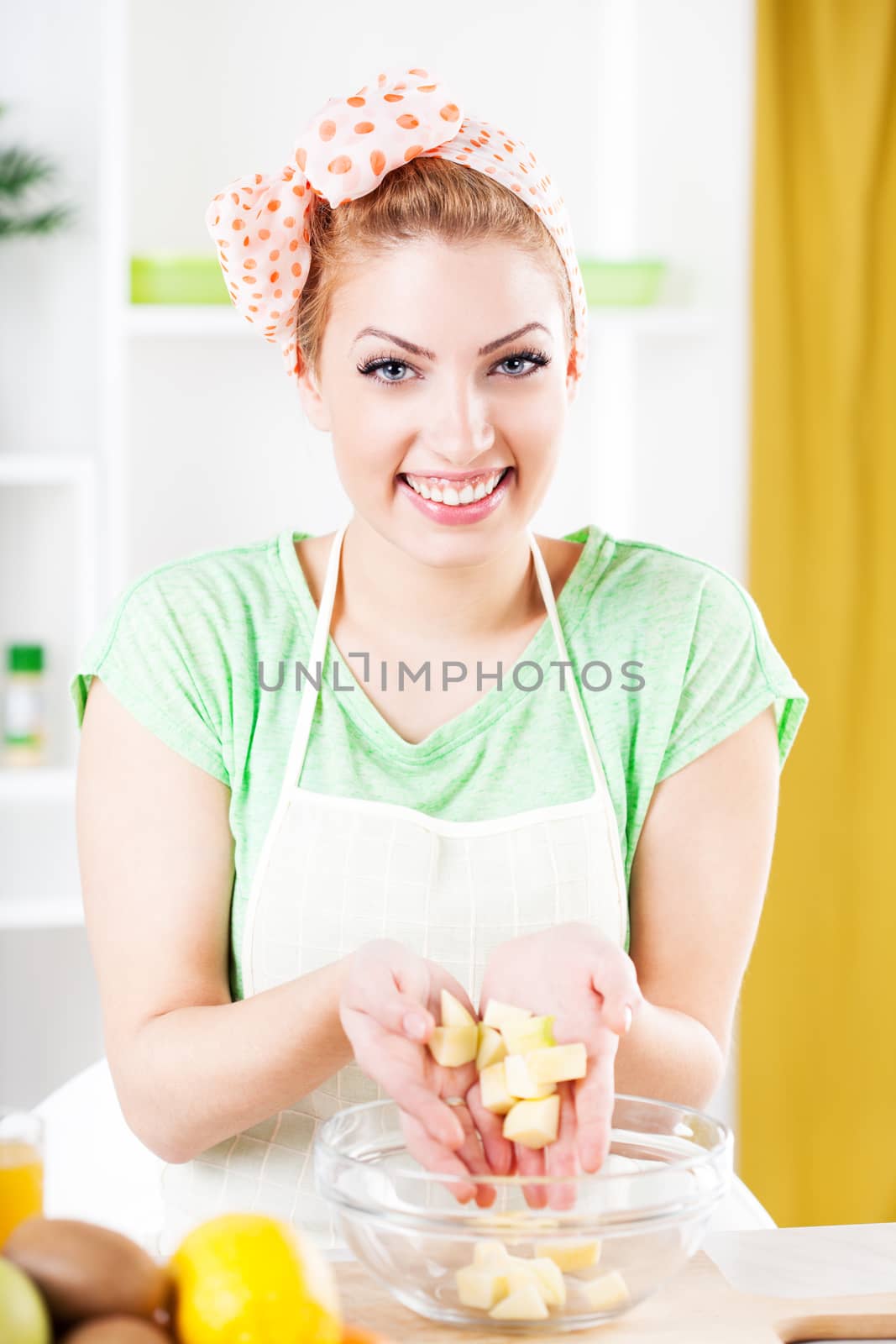 Beautiful young woman preparing apple for fruit salad in a kitchen. Looking at camera.