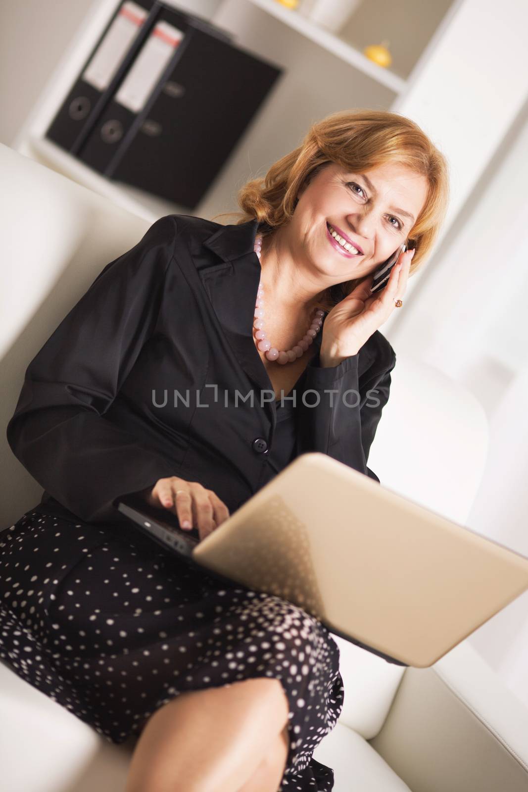 Happy Senior businesswoman working on laptop and talking on mobile phone.