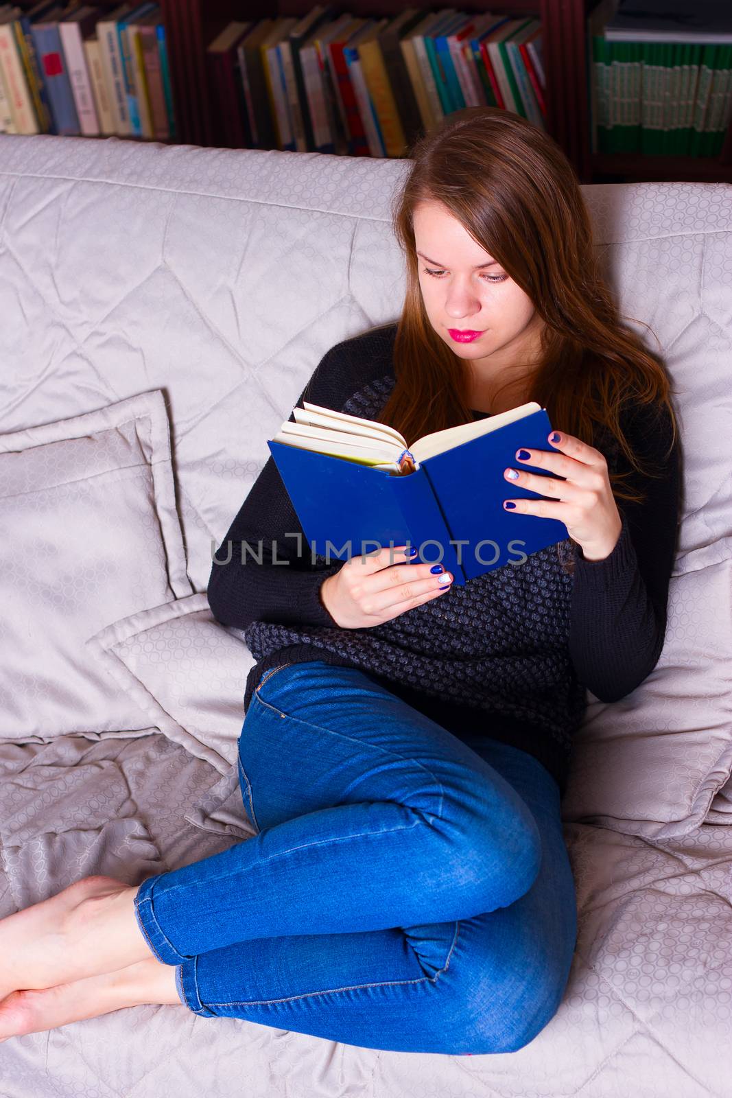 young woman sitting on sofa at home, reading a book  by victosha