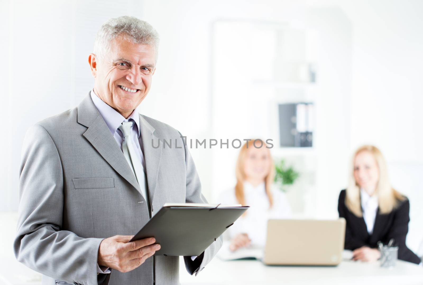 Happy senior businessman with documents standing in the office. Looking at camera. Selective Focus.