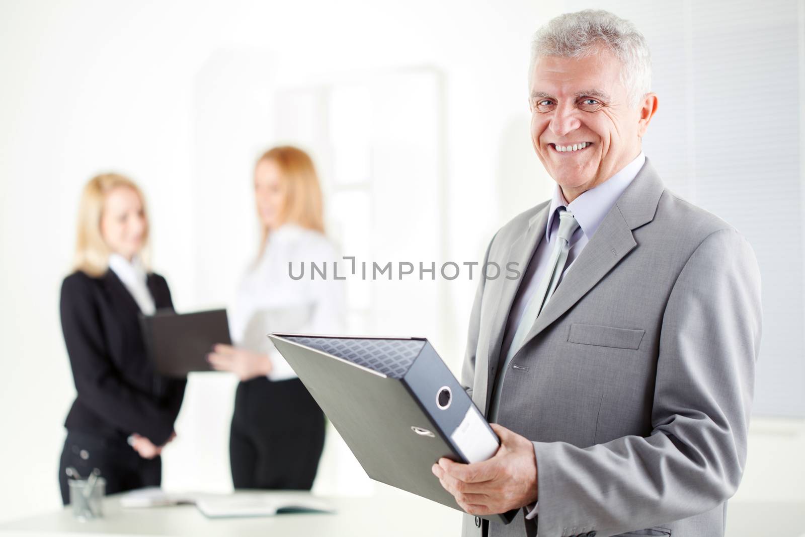 Happy senior businessman with documents standing in the office. Looking at camera. Selective Focus.