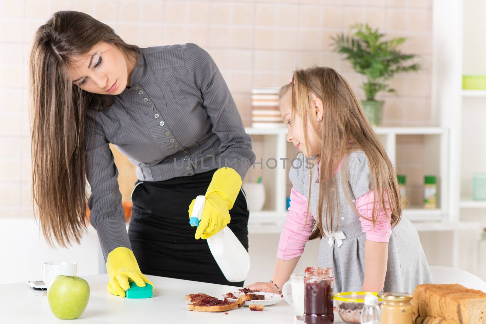 Angry Overworked businesswoman cleaning table in the morning and late for work, because her Daughter making mess with jam.