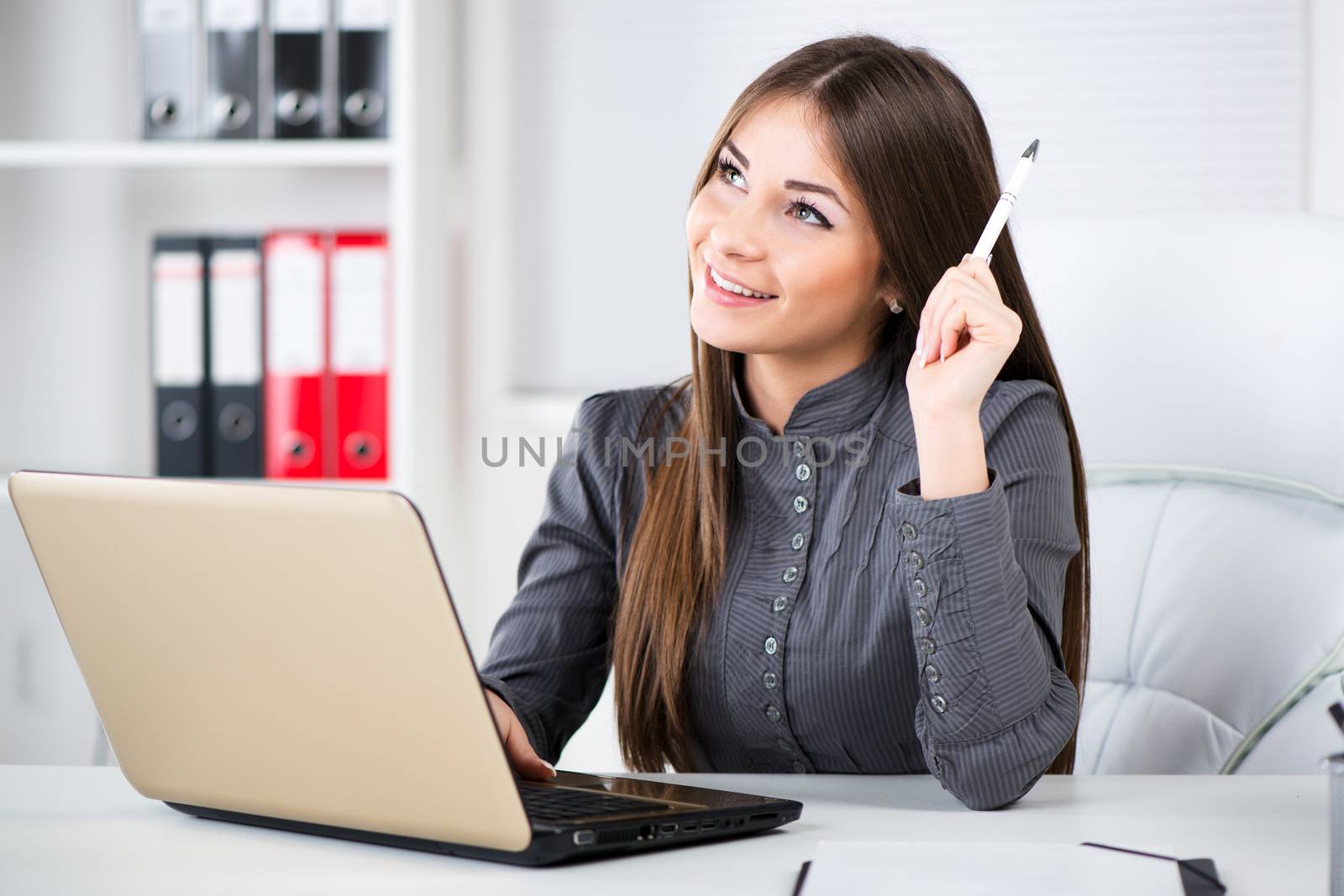 Businesswoman in the office, sitting, thinking and holding pencil in one hand.