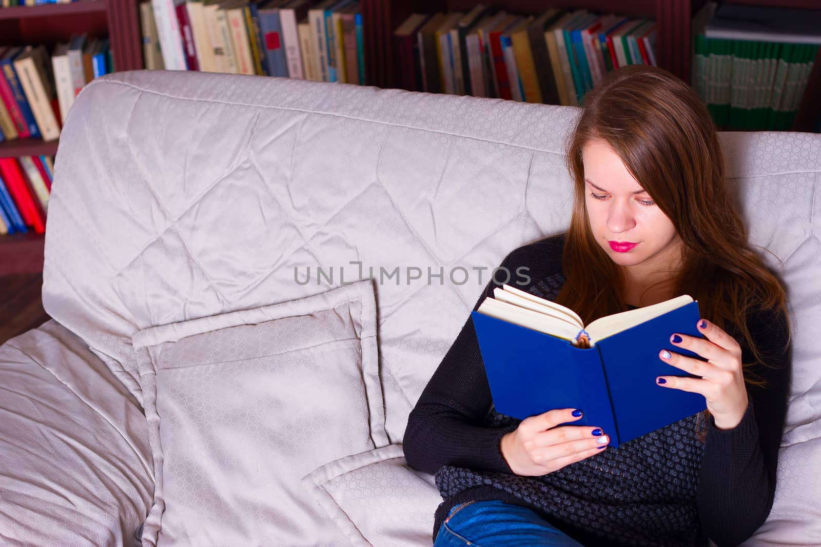 young woman sitting on sofa at home, reading a book  by victosha