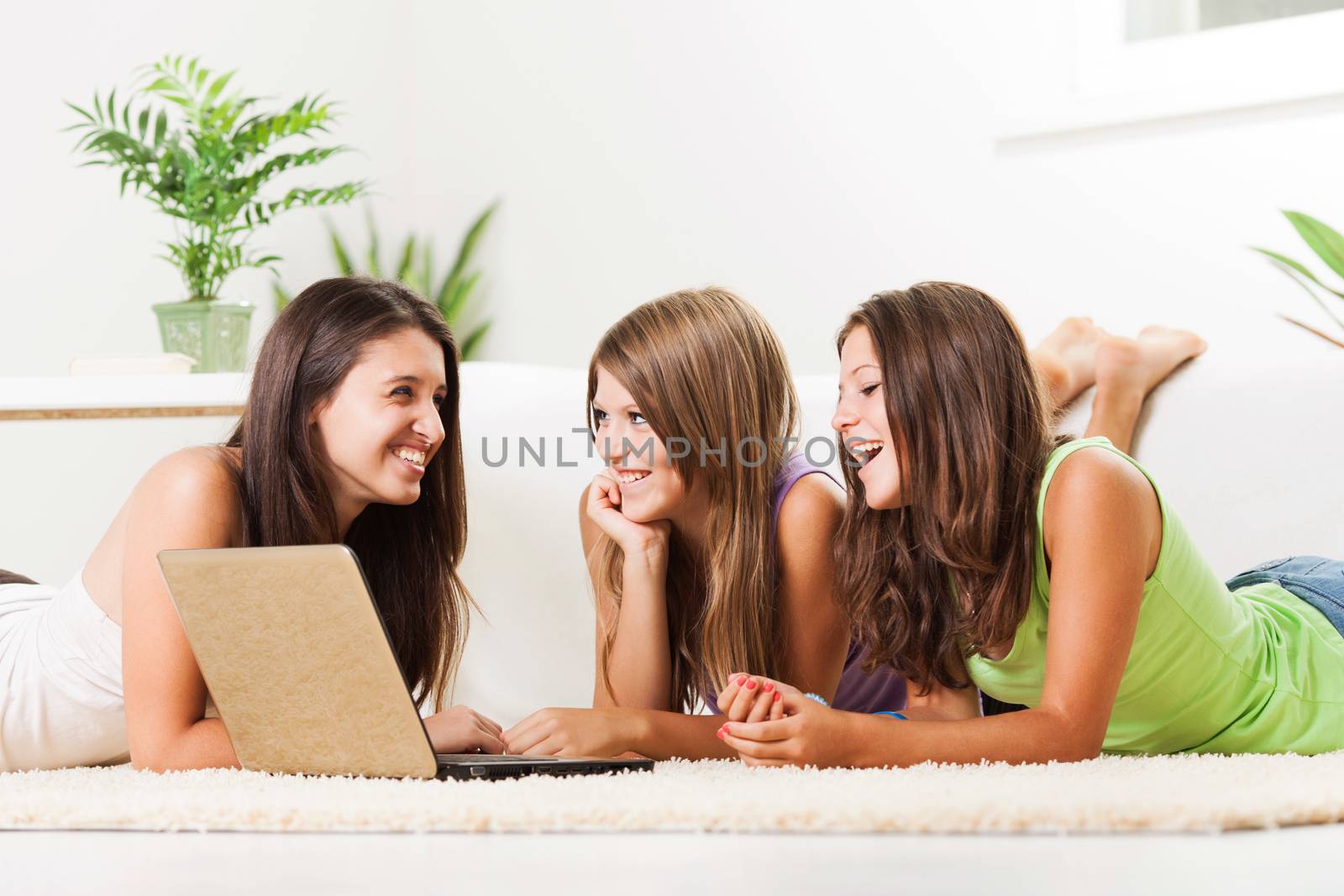 Three Beautiful teenage girls lying on the carpet and surfing internet on laptop