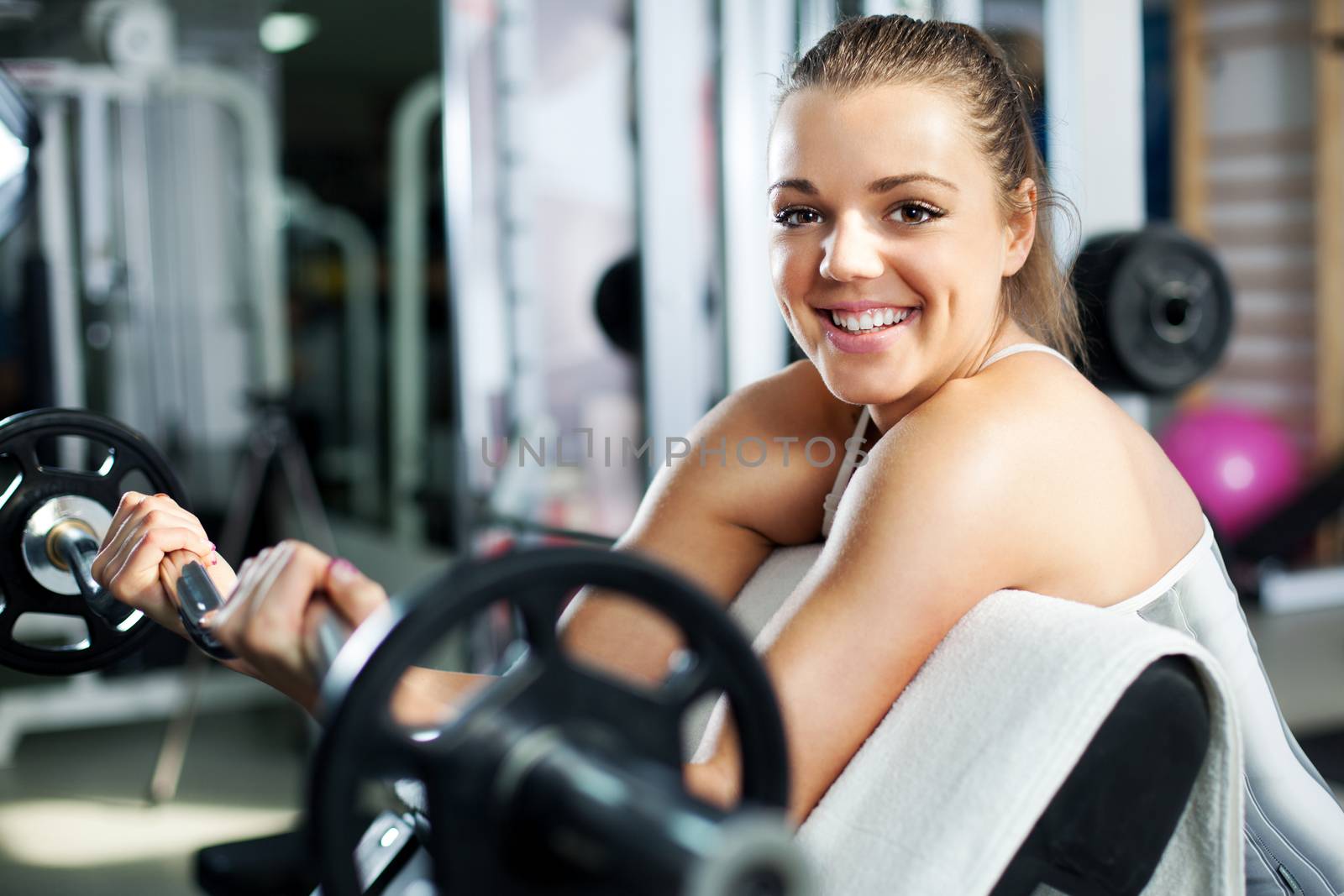 Cute Sporty young woman doing exercise in a fitness center. She is working exercises to strengthen her bicep.