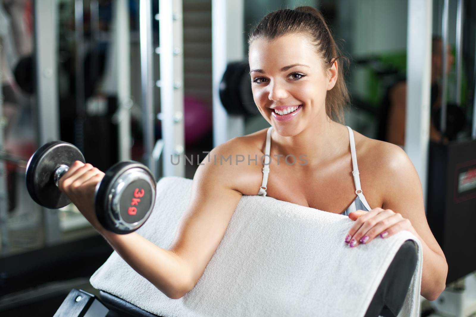 Cute Sporty young woman doing exercise in a fitness center. She is working exercises to strengthen her biceps.