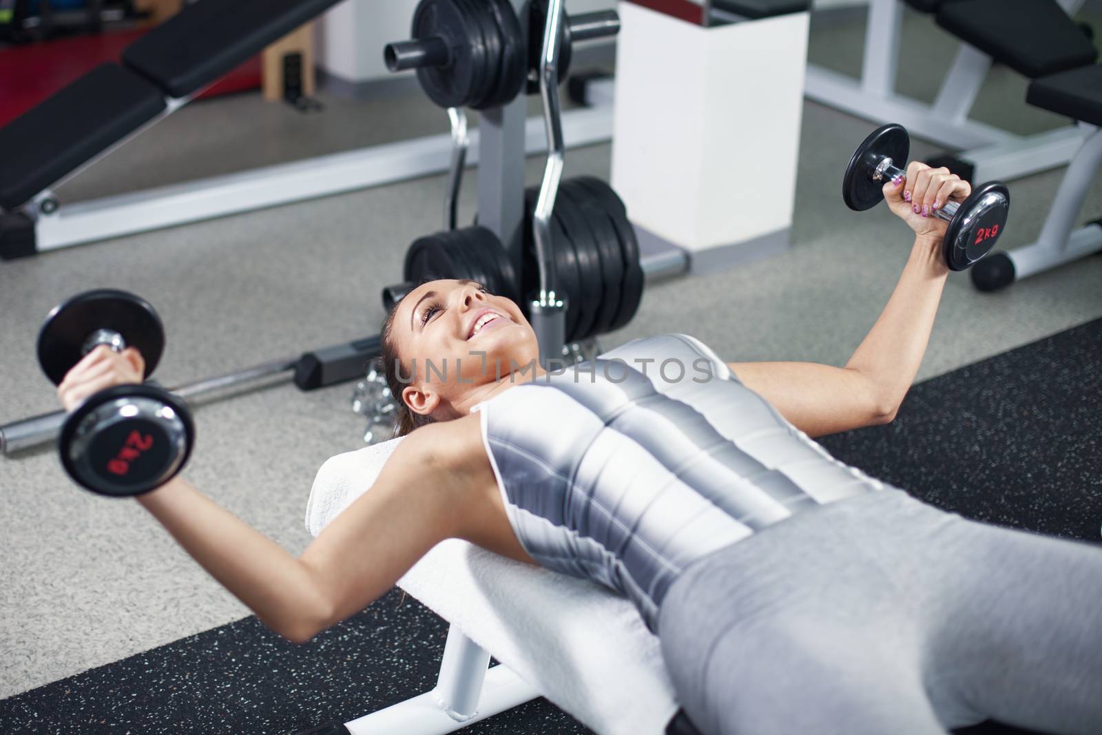 Cute Sporty young woman doing exercise in a fitness center. She is working exercises to strengthen her chest.