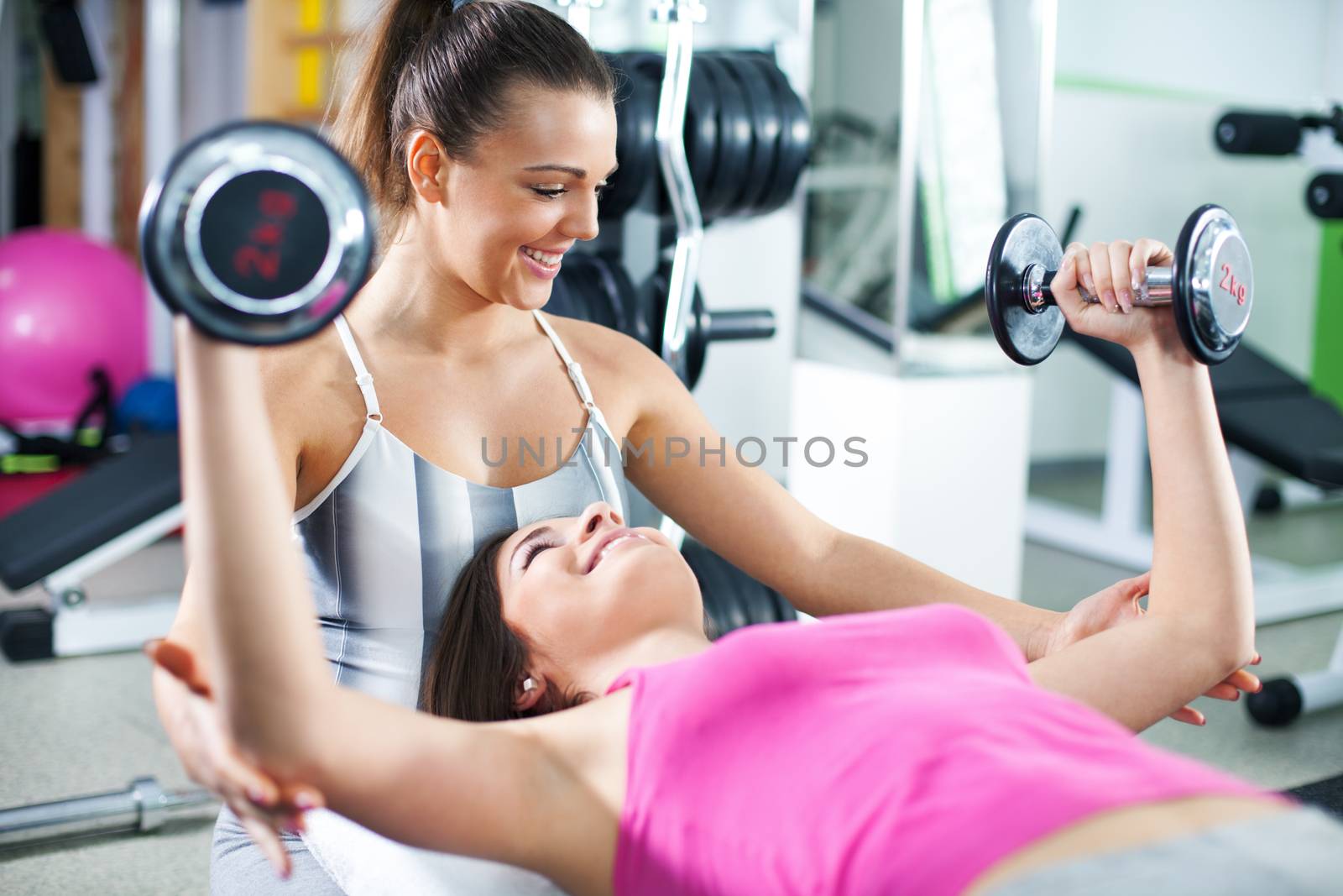 Cute Sporty young woman doing exercise in a fitness center with her personal coach. She is working exercises to strengthen her chest.