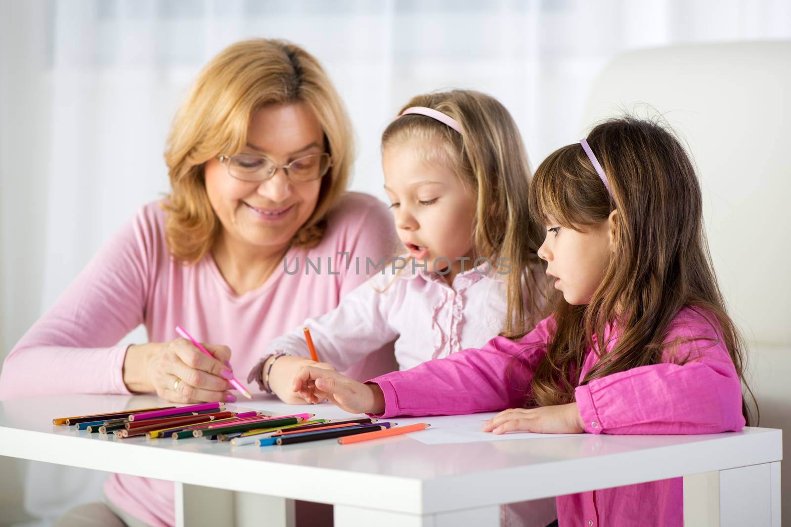 Two Cute little girls drawing with colored pencils at home with Grandmother.