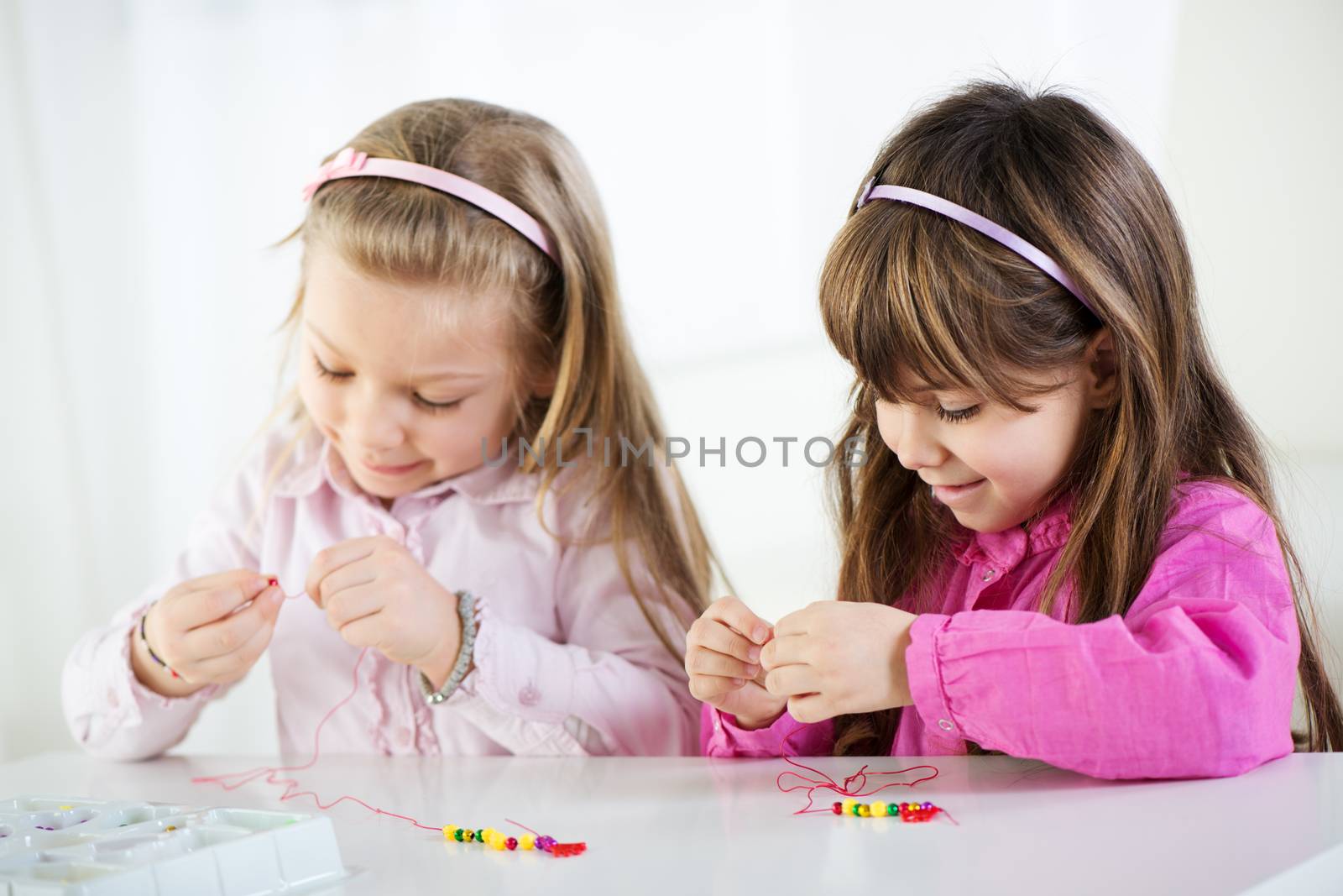 Two Cute little girls making bead Jewelry at home.