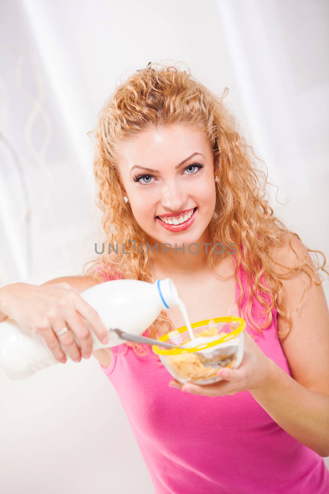 Beautiful young woman eating milk and corn flakes for breakfast