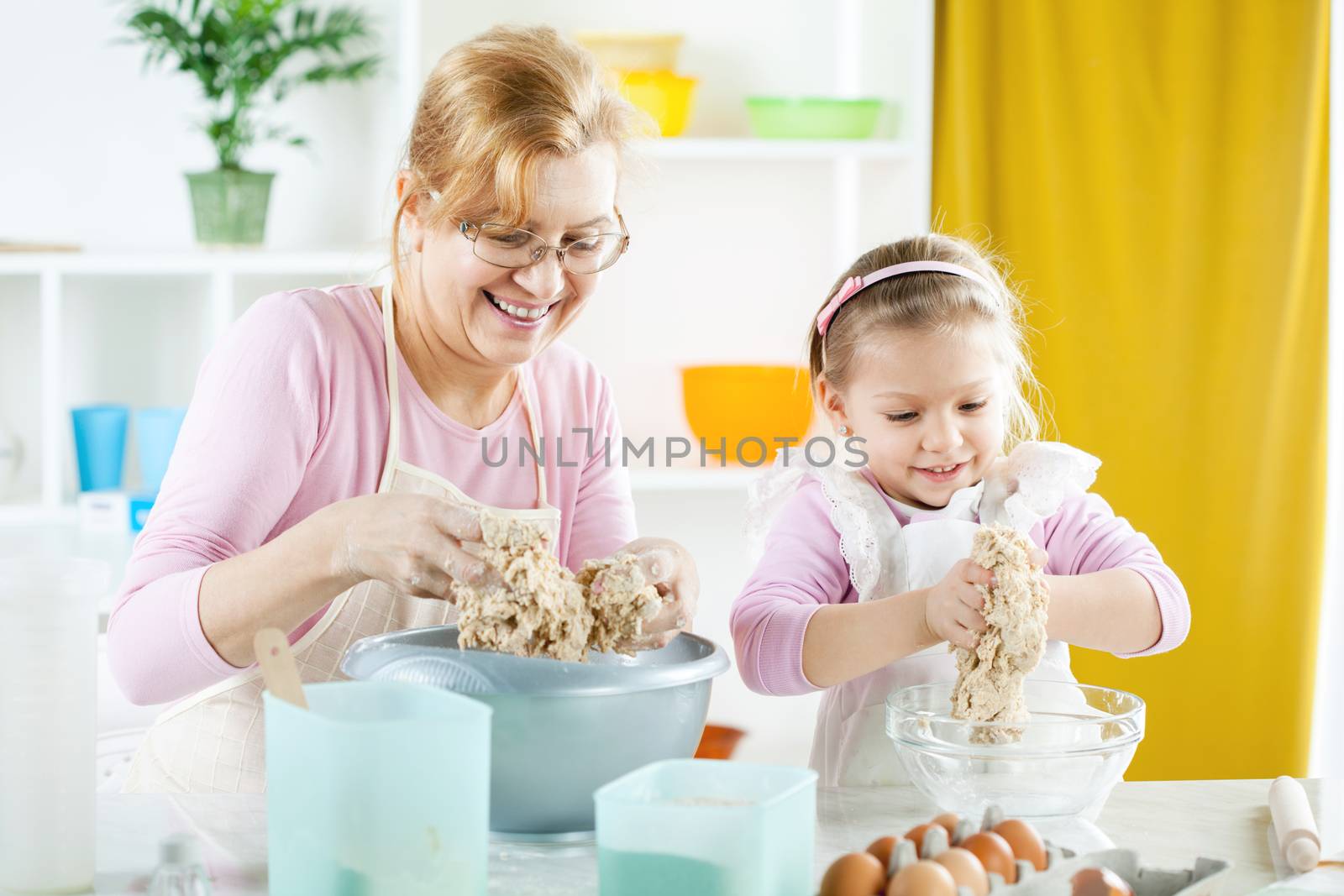 Beautiful happy grandmother learning her granddaughter how making Dough in the kitchen.