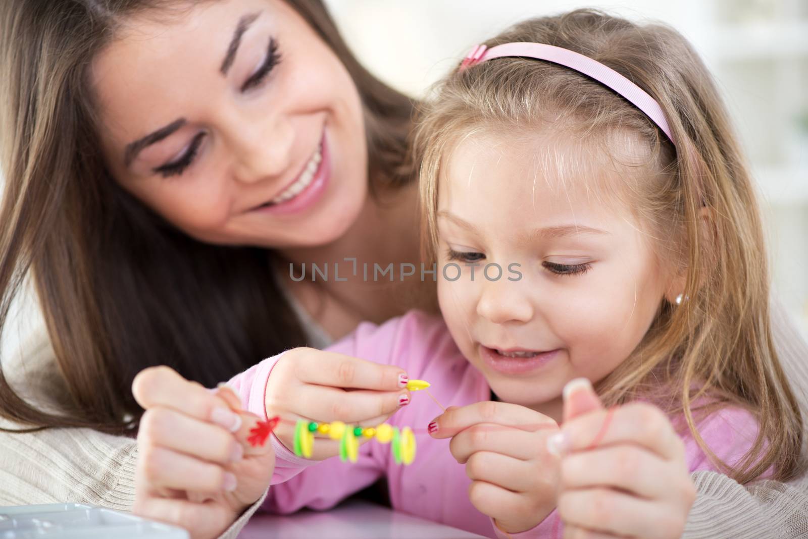 Mother and daughter playing at home. They Making bead bracelets.