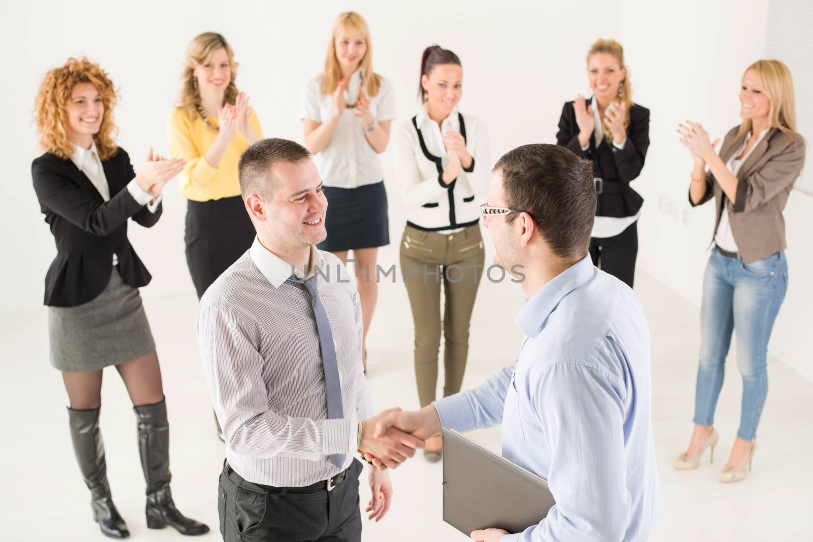 Two successful businessmen shaking hands at the meeting. Group of their colleague celebrating in the background.