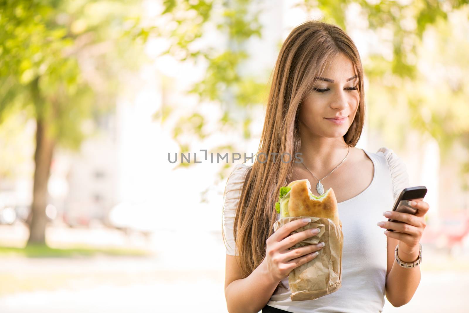 Portrait of beautiful young woman taking a break for breakfast and using a Cell Phone Outdoors.