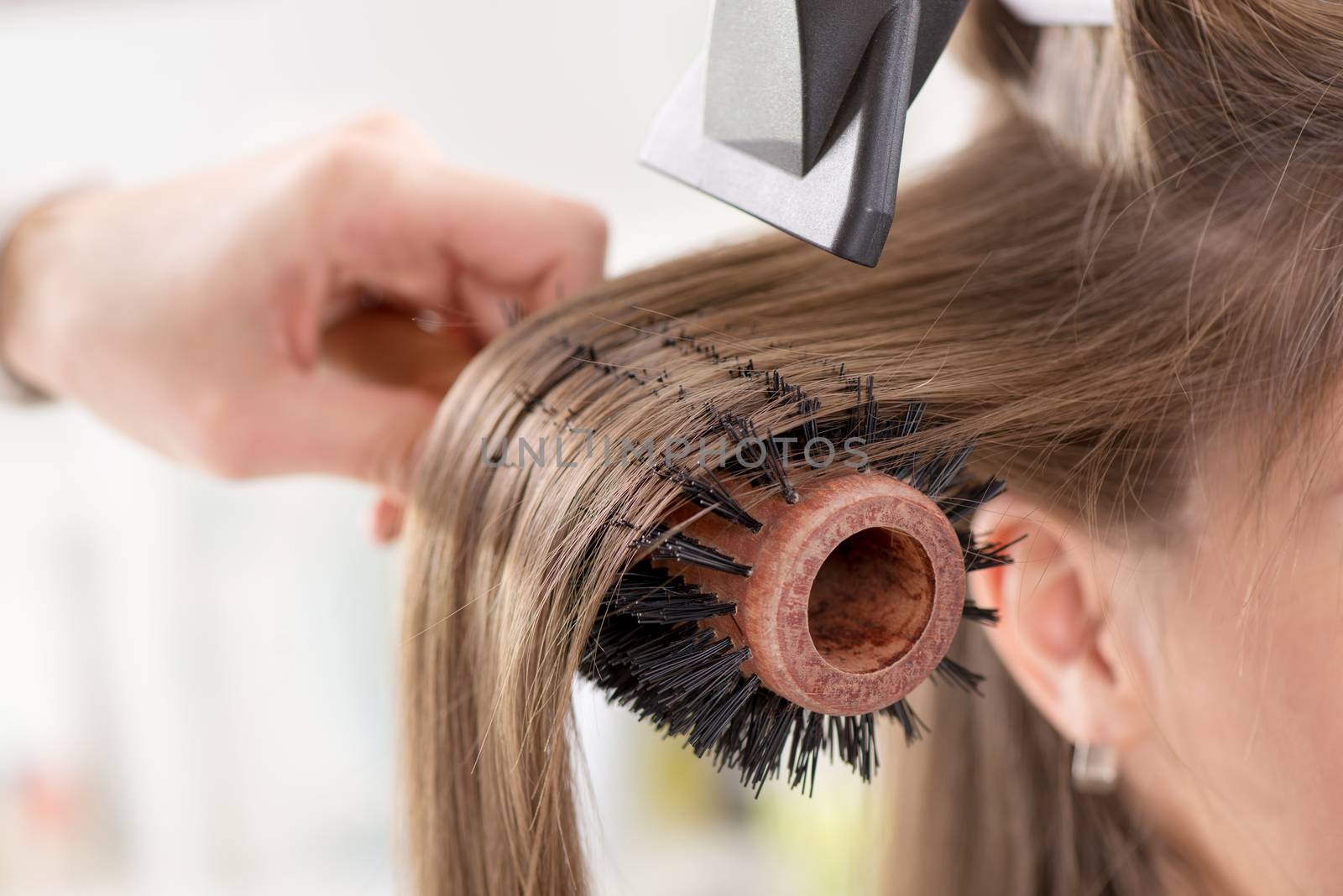 Drying long brown hair with hair dryer and round brush. Close-up.