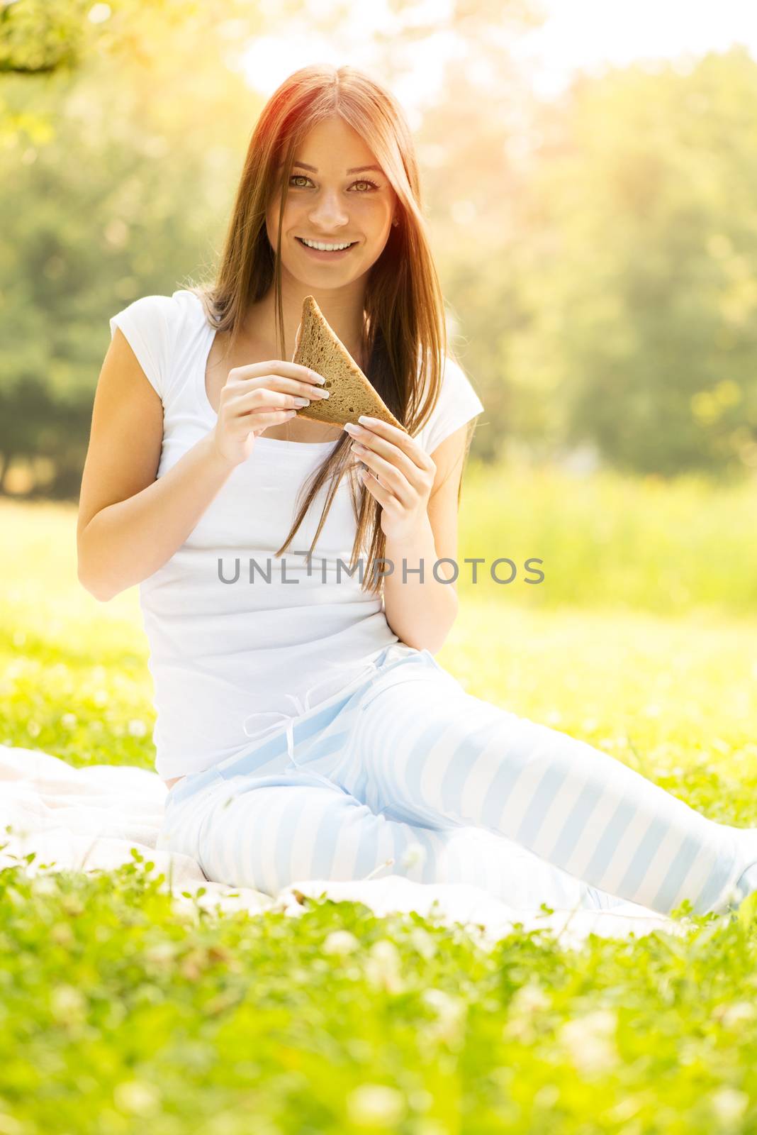 Beautiful girl eating sandwich and sitting on the grass in the park.