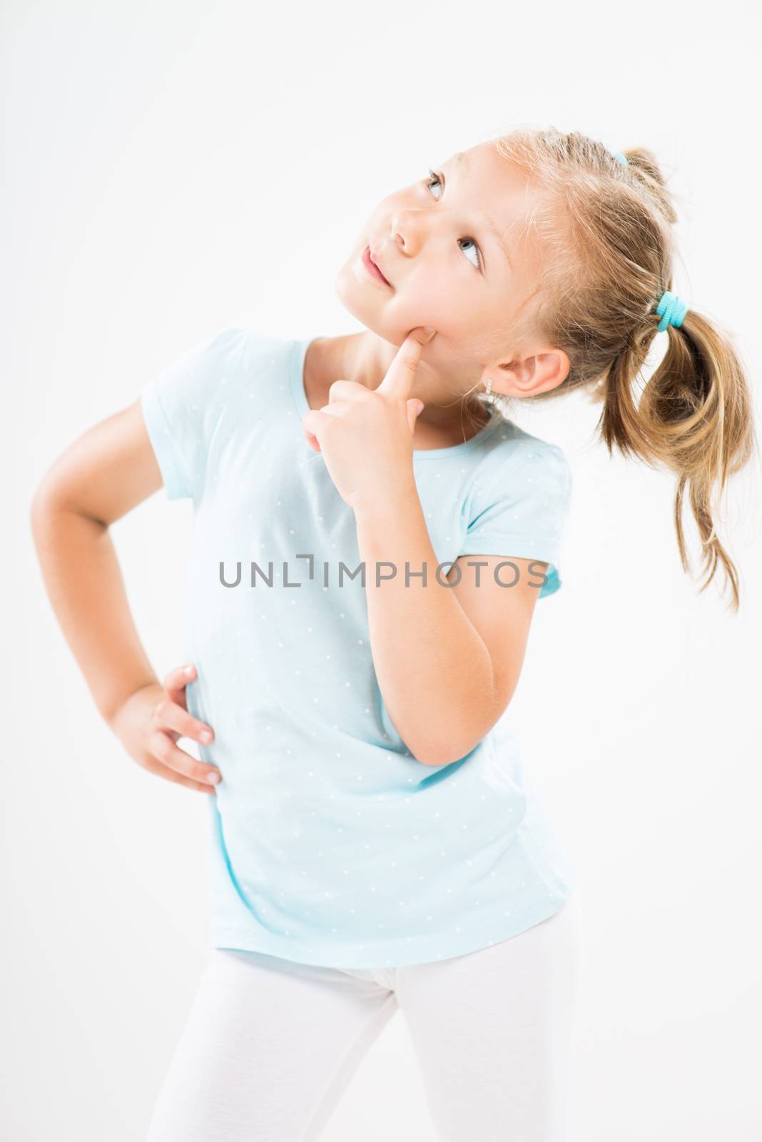 Cute little girl standing against a white background and thinking...