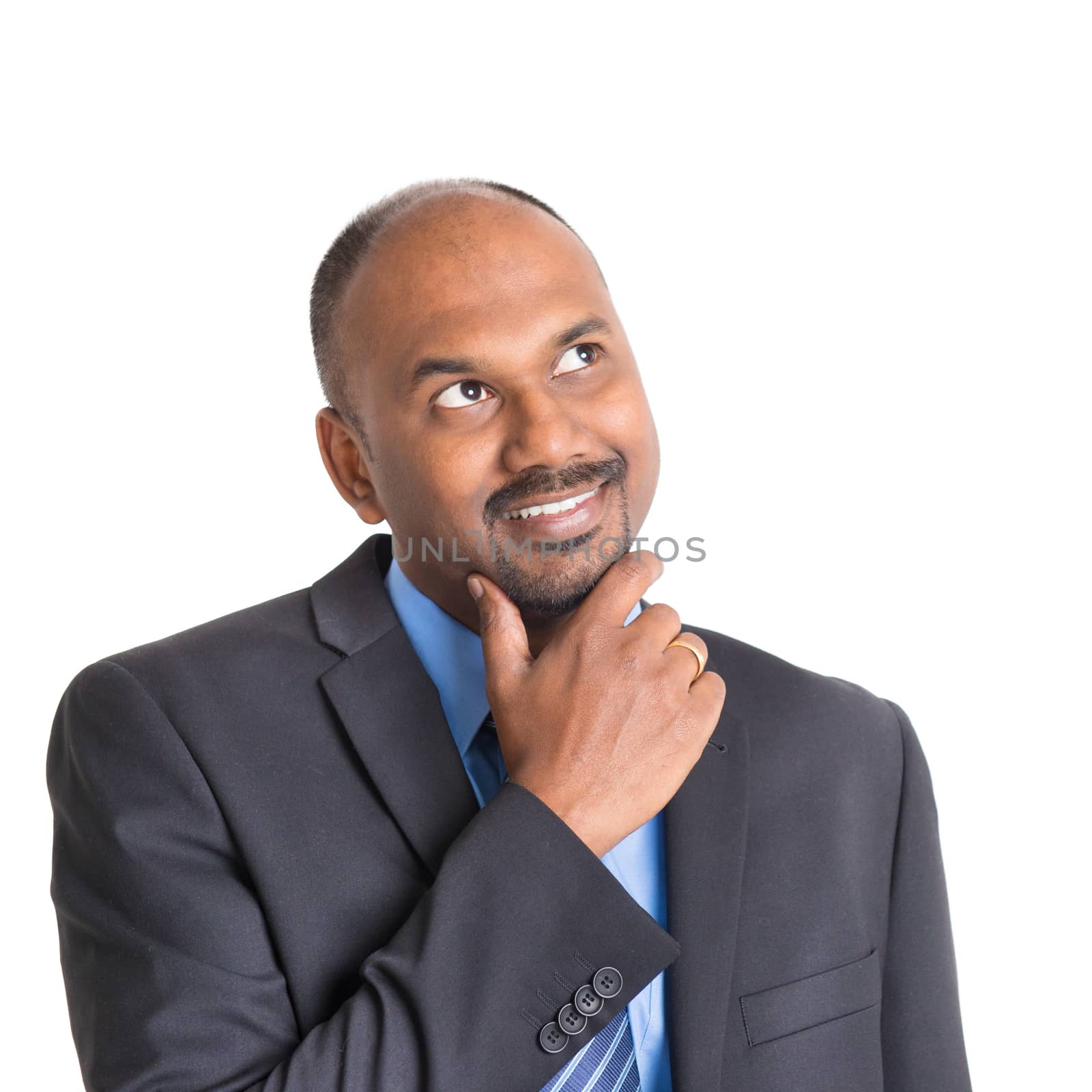 Portrait of mature Indian businessman looking up smiling and thinking, standing on plain background with shadow.