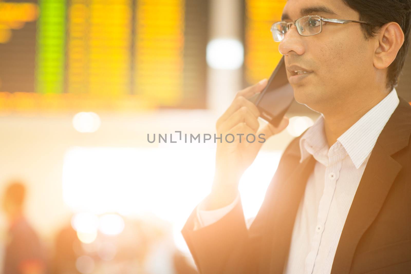 Asian Indian Business man on the phone during his business travel, at the airport, golden sun light background.