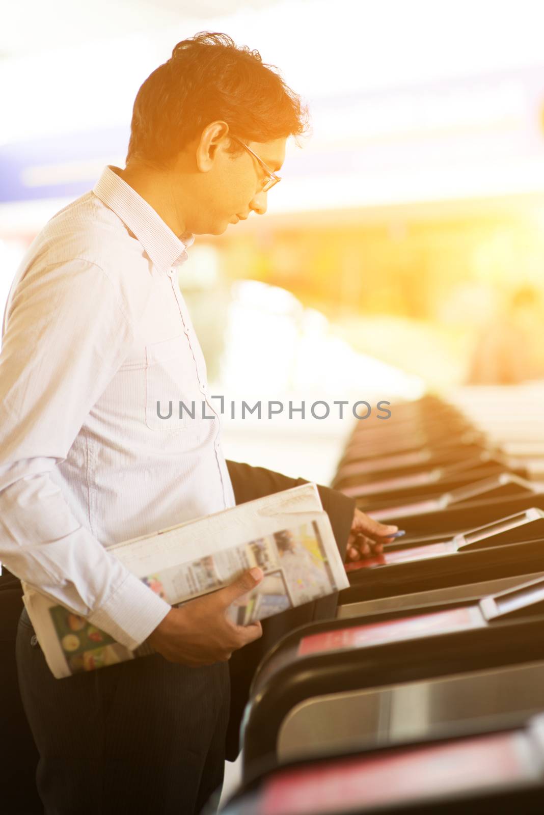 Asian Indian businessman at entrance of railway station, touching ticket token on gate barrier during sunset, beautiful golden sunlight background.