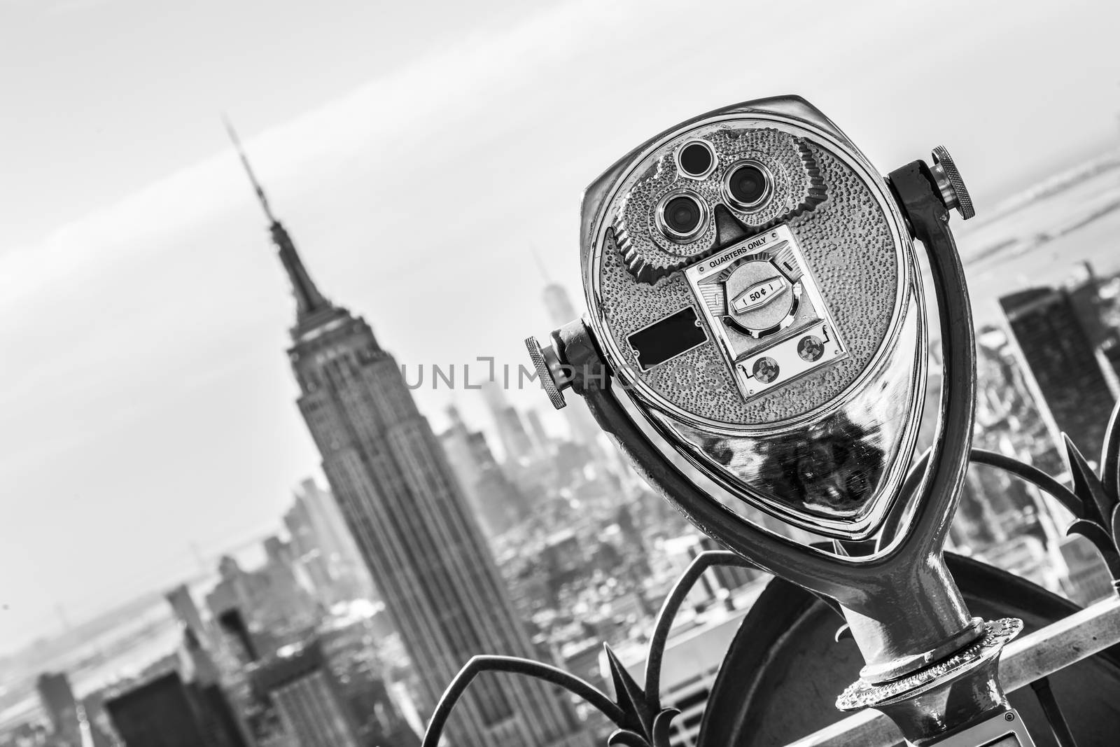 New York City, USA. Vintage tourist binoculars at Top of the Rock observation deck in front of Manhattan downtown skyline with Empire State Building and skyscrapers at sunset. Black and white.