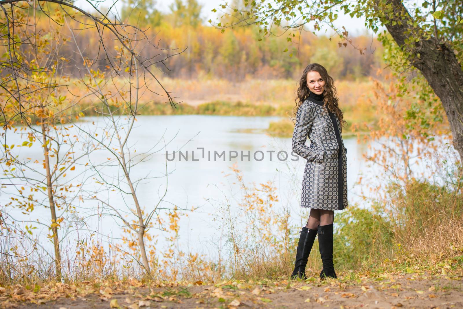 A young girl walks by the river in the autumn forest by Madhourse