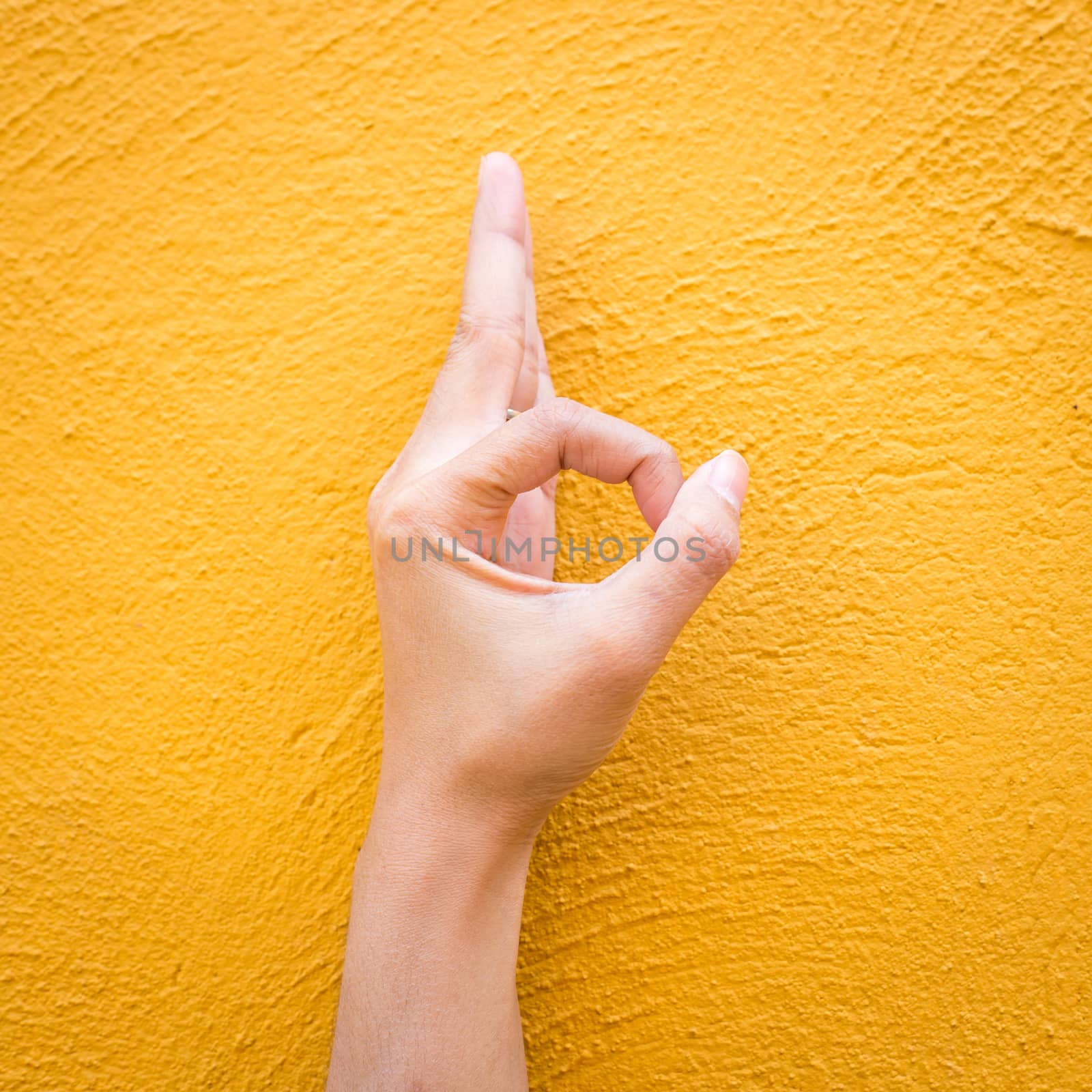 Woman hand in ok sign on cement yellow wall background