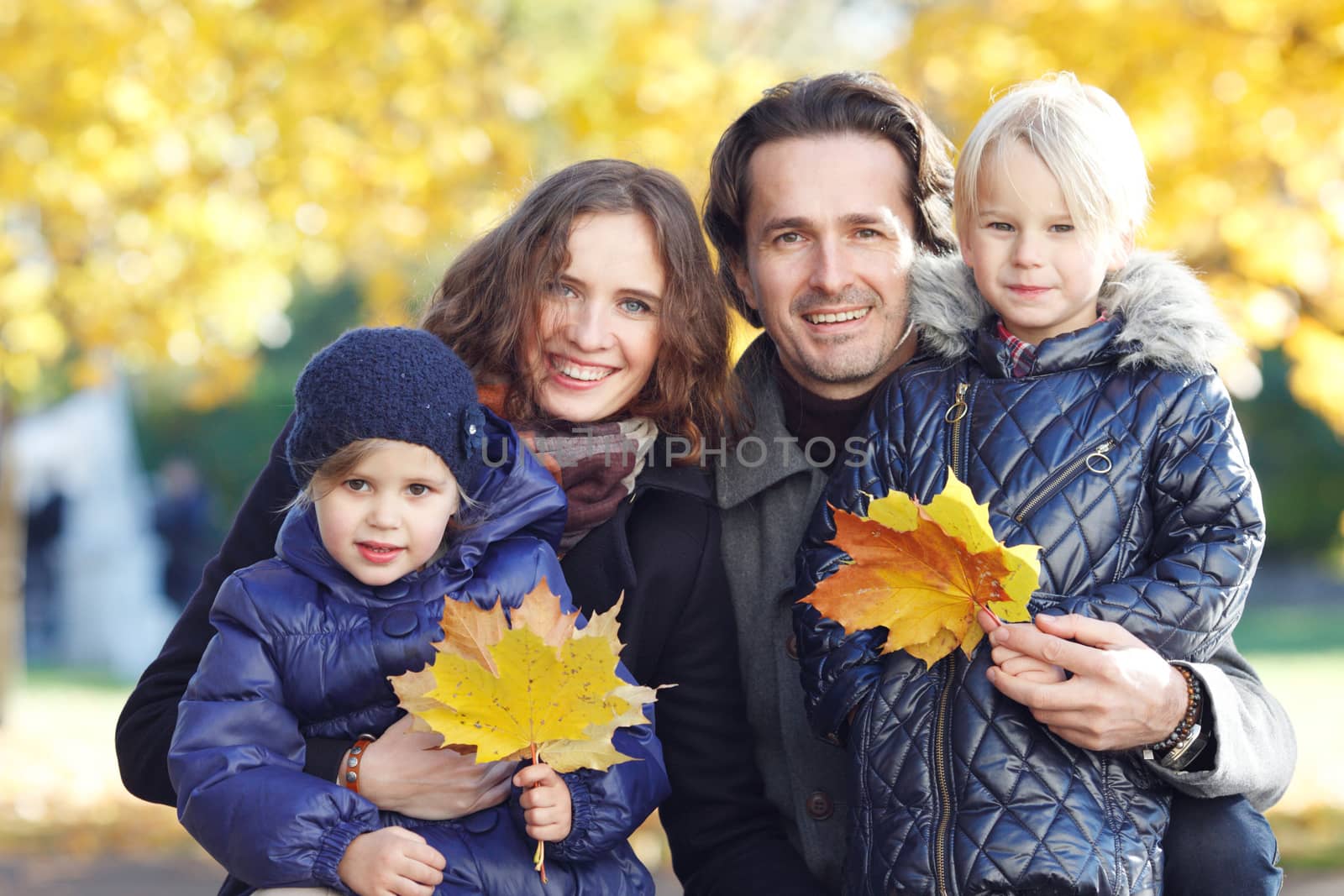 Portrait of a happy family in autumn park with maple leaves