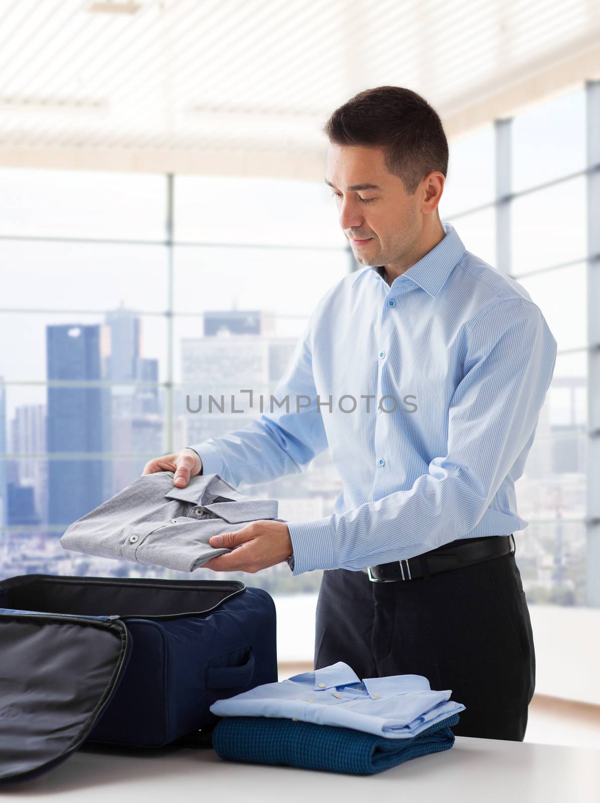 business, trip, luggage and people concept - happy businessman packing clothes into travel bag over home or hotel room background