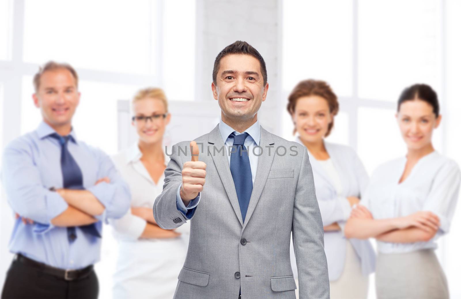 business, people, gesture and office concept - happy businessman with team over office room background showing thumbs up