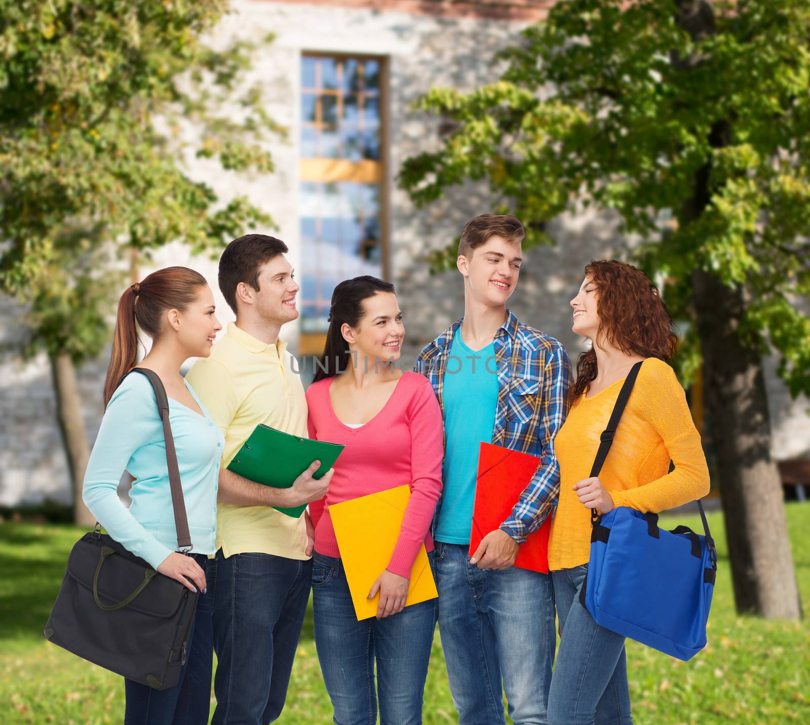 friendship, school, education and people concept - group of smiling teenagers with folders and school bags over campus background