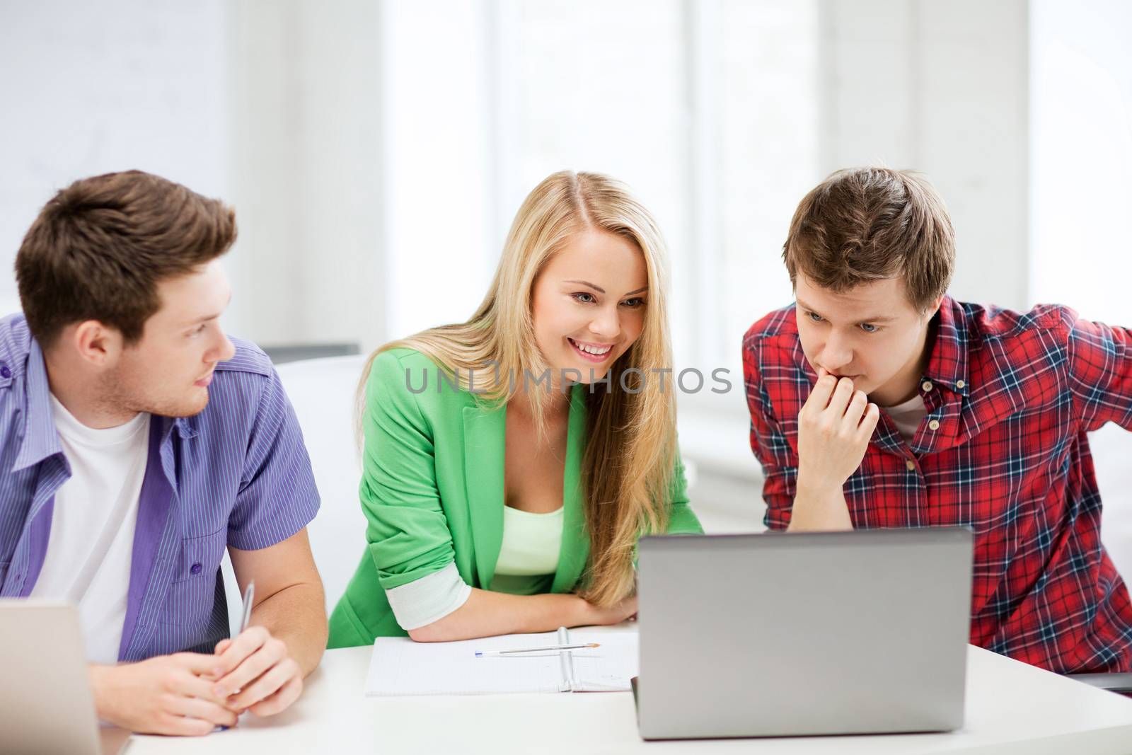 education concept - smiling students looking at laptop at school