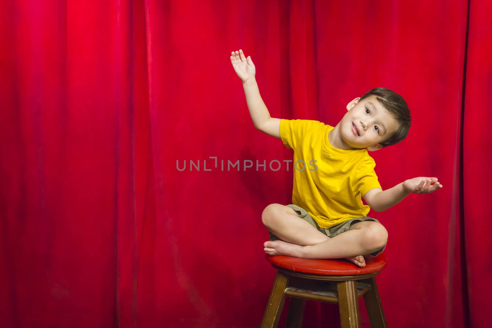 Handsome Mixed Race Boy Sitting on Stool in Front of Red Curtain.