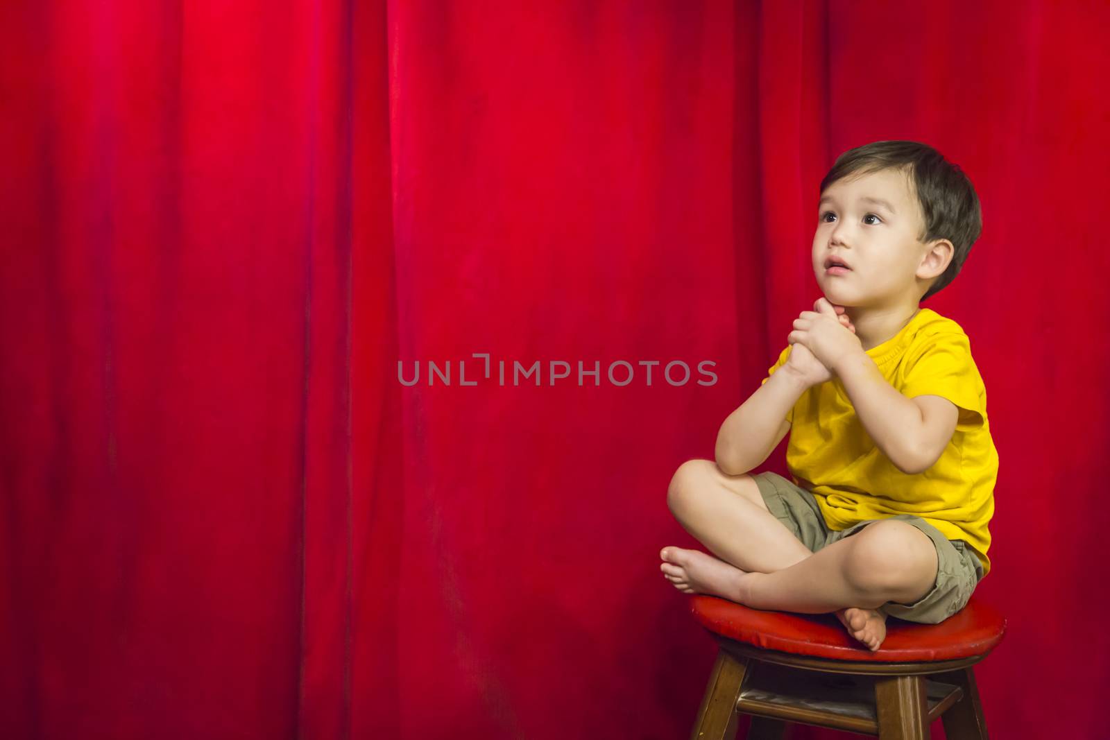 Handsome Mixed Race Boy Sitting on Stool in Front of Red Curtain.