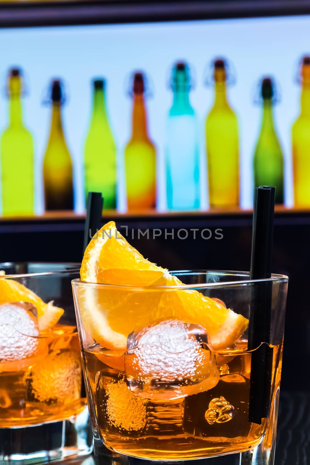 detail of two glasses of spritz aperitif aperol cocktail with orange slices and ice cubes on bar table, disco atmosphere background, lounge bar concept