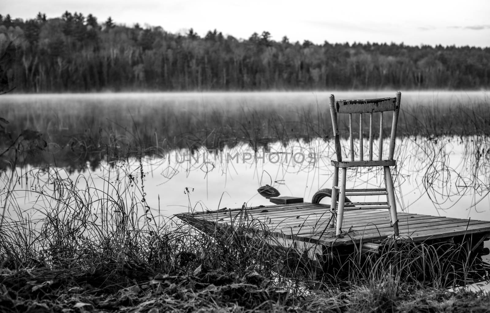 Morning reveals fog and a chair sits on a partially submerged dock beside a lake in Ontario, Canada.