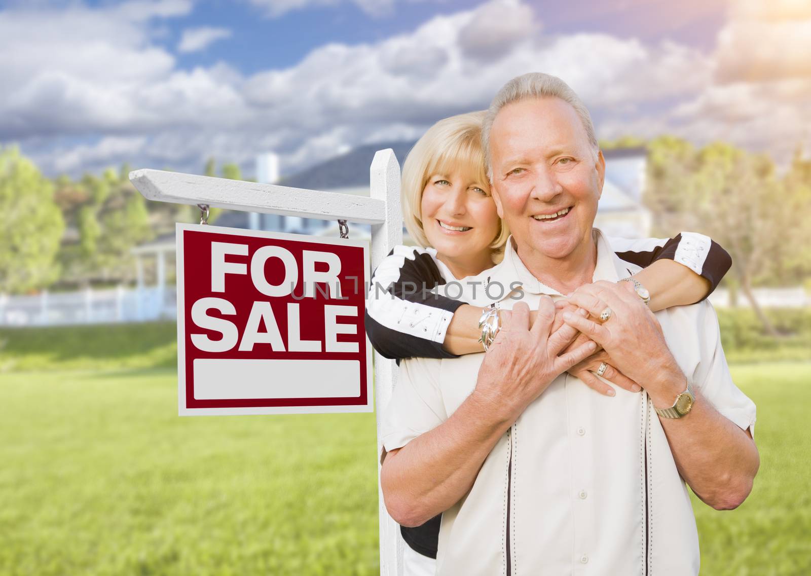 Happy Senior Couple Front of For Sale Real Estate Sign and House.