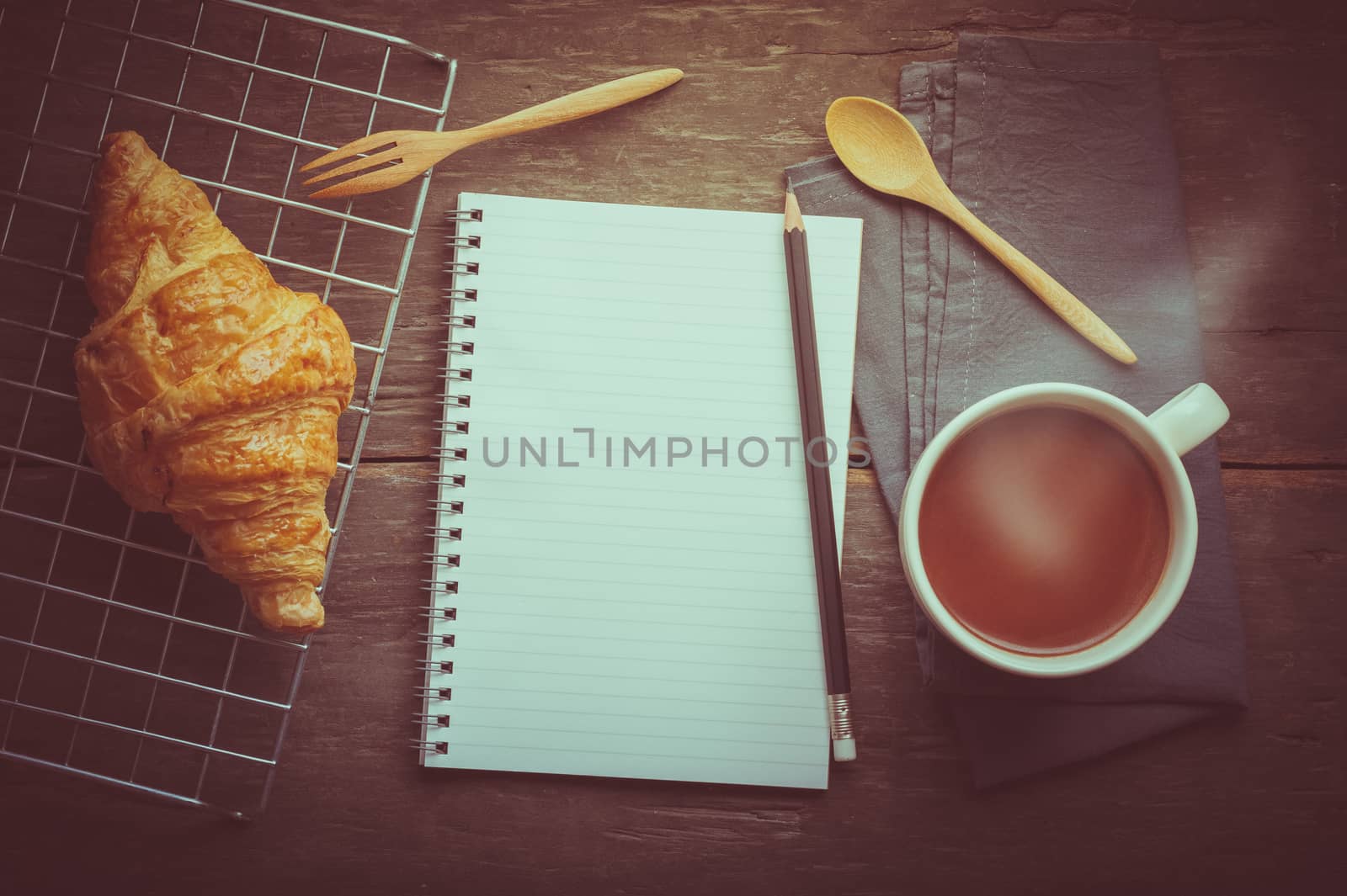 Butter croissant with a cup of hot chocolate and small notebook with blank area for text or message on wood table in morning time with film filter effect