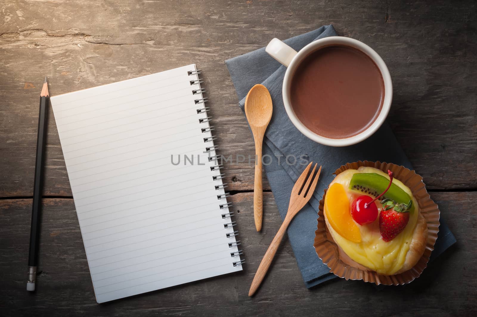 Fruit danish pastry with hot chocolate and opened notebook with blank area for text or message on wood table in morning time