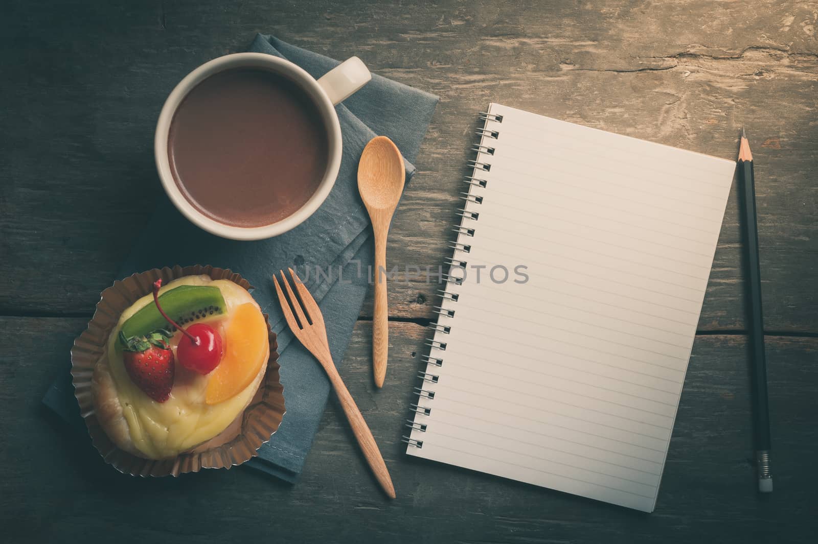 Fruit danish pastry with hot chocolate and opened notebook with blank area for text or message on wood table in morning time with film filter effect