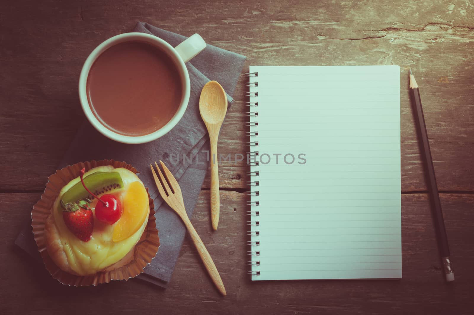 Fruit danish pastry with hot chocolate and opened notebook with blank area for text or message on wood table in morning time with film filter effect