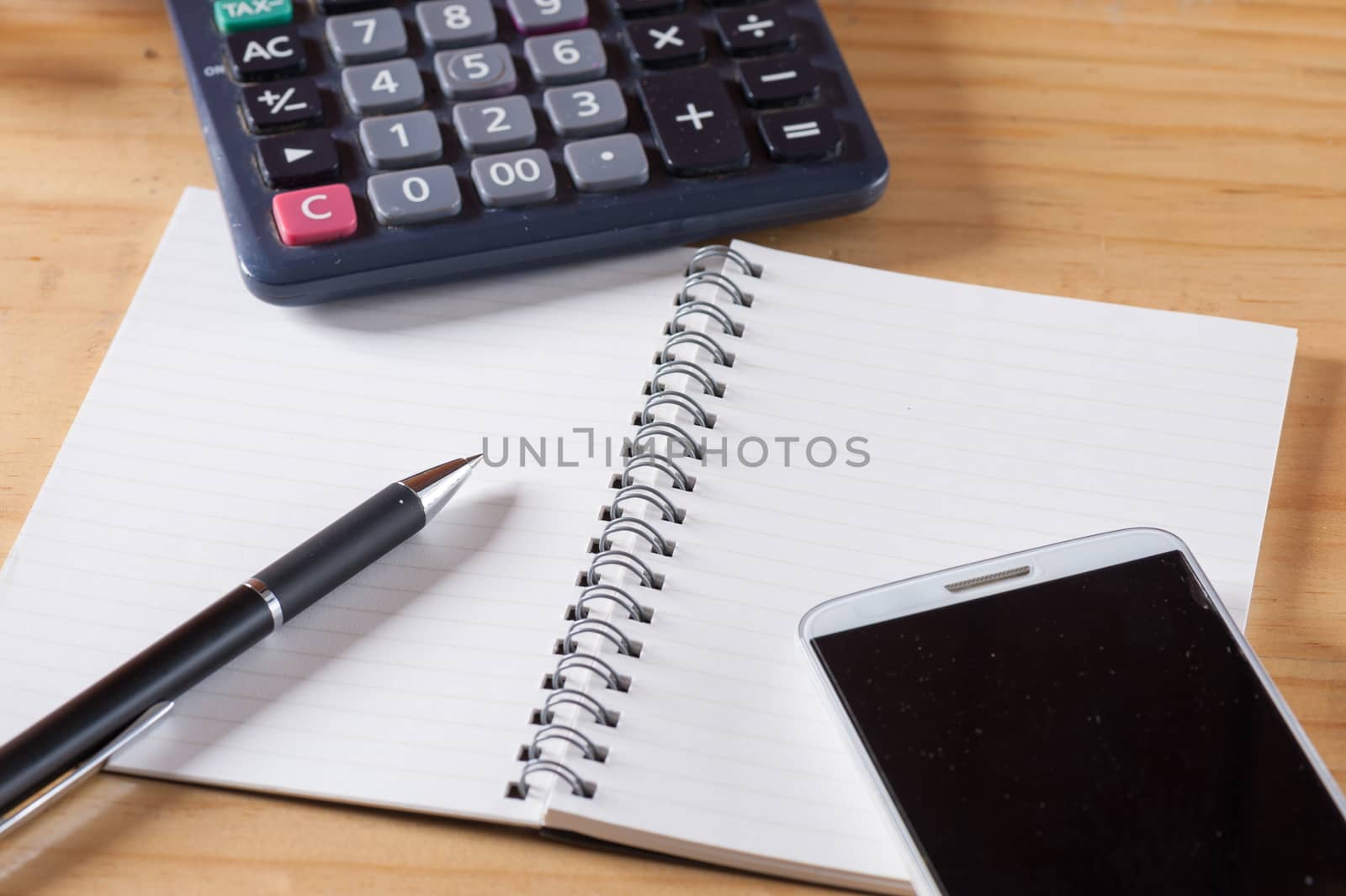 Opened notepad with blank area for text or message, pen, smart phone, and calculator on wood table