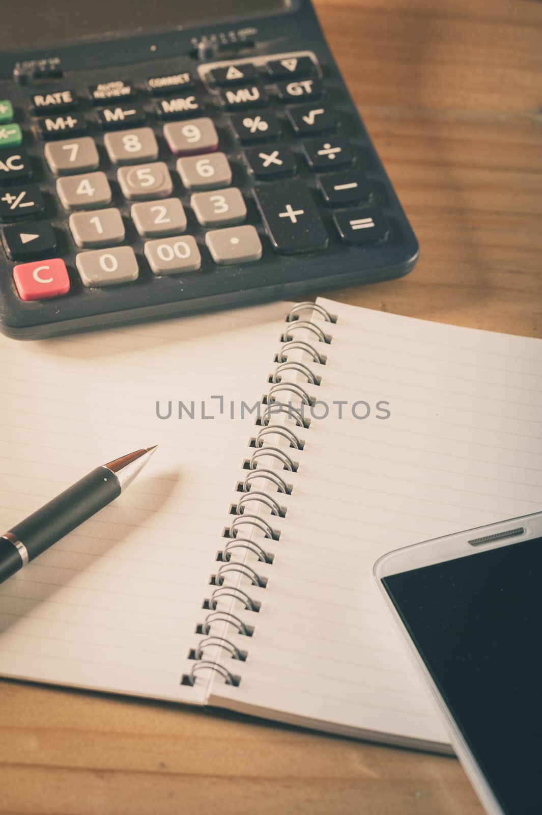 Opened notepad with blank area for text or message, pen, smart phone, and calculator on wood table with film filter effect