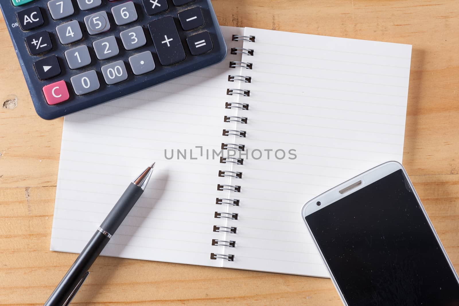 Opened notepad with blank area for text or message, pen, smart phone, and calculator on wood table
